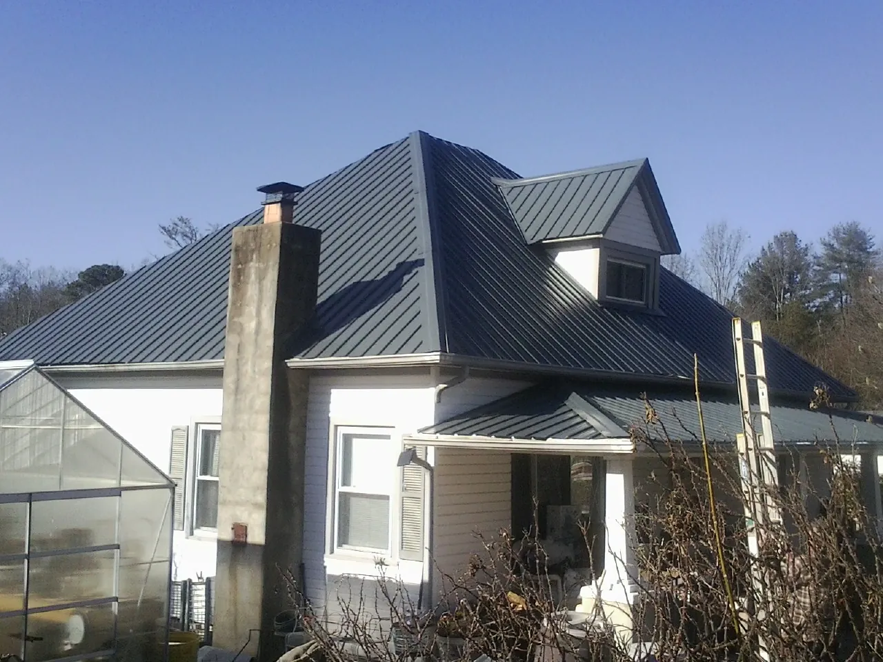 Dark blue standing seam metal roof on a white farmhouse with dormer — Slate & Tile Roof Repair by Roofing Brothers in Readyville