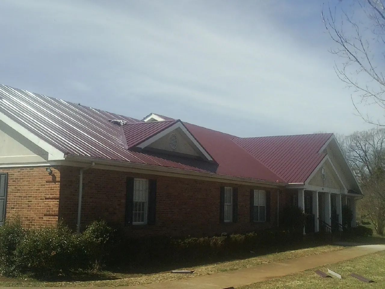 Red metal roof with gabled entries on a long brick building, from a Hail Damage Roof Repair job in Readyville