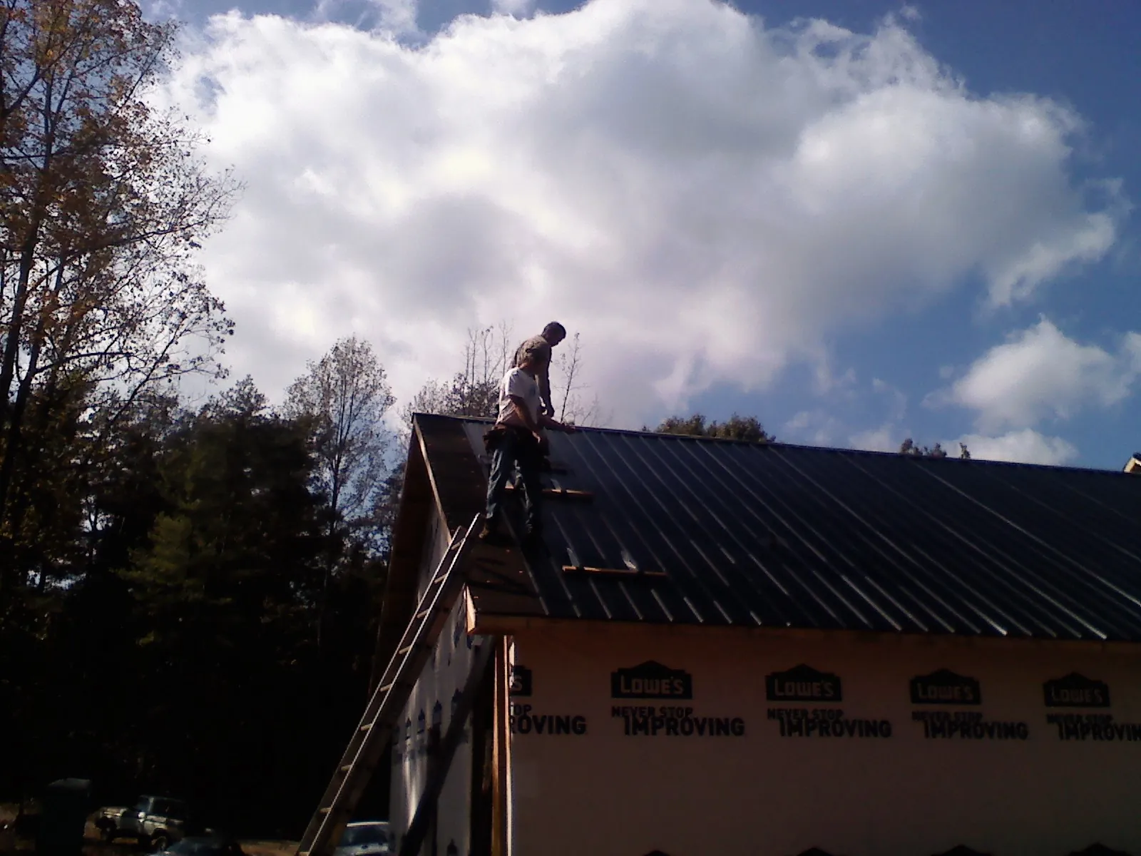 Roofer fastening dark metal panels high against a cloudy sky, from a Roof Inspection job in Readyville