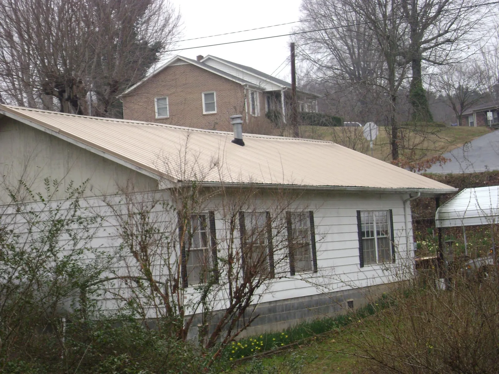 Tan metal roof on a white sided house set into a hillside — Commercial Roofing by Roofing Brothers in Readyville